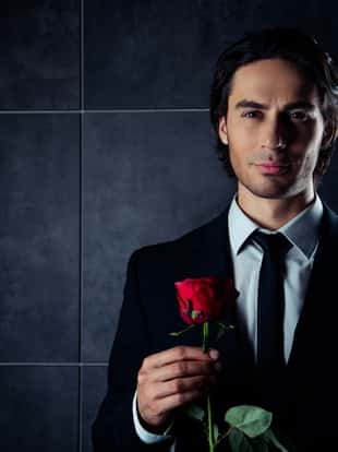 portrait of handsome romantic young man in formalwear  holding red rose