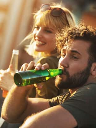 Closeup of a young couple having some beers on a rooftop terrace on a hot summer afternoon ad looking down the street.