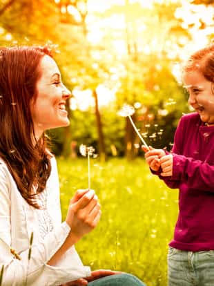 Mother with small daughter blowing to dandelion - lifestyle outdoors scene in park