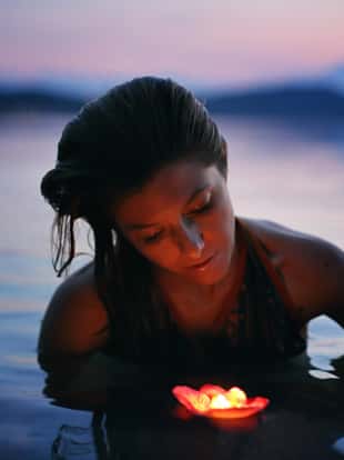 Beautiful woman with floating candle in purple lake waters . Beauty and romance concept