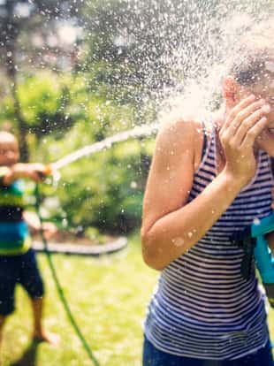 Little boy is splashing his sister with garden hose. Sunny summer day.Nikon D810