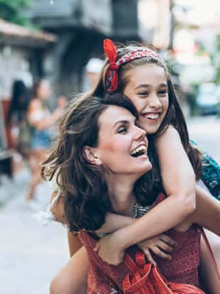 Mother and little girl having fun in piggyback ride outdoors.