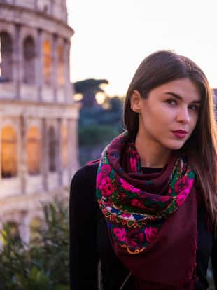 Russian girl posing in front of the Colosseum in Rome. The girl is wearing a typical Russian traditional foulard, with bright colors and red flowers. In the background behind it is the imposing Flavian Amphitheater, better known as the Roman Coliseum.
