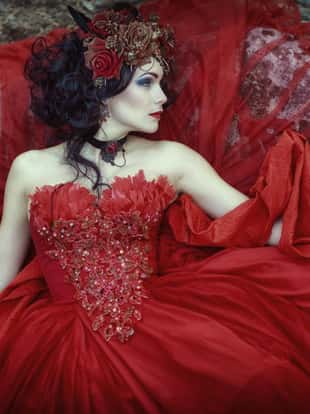 Queen in a red dress is lying on a rock in the woods