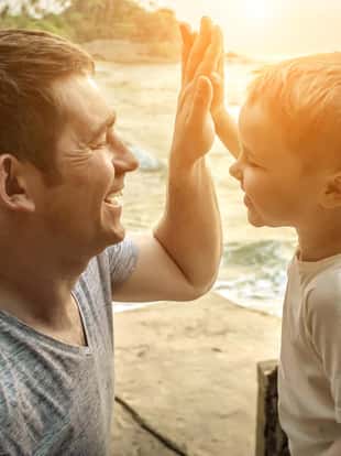 Happiness Father and son stay on the sea costline. Tropical beach under sunset sky with sun. Summer holidays.