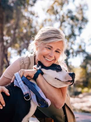 Happy senior woman enjoying walk in nature and embracing pet dog in forest park
