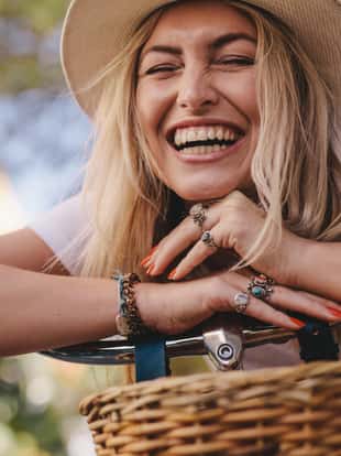 Attractive woman leaning on her bike and laughing. Female wearing hat looking happy with her bicycle outdoors.