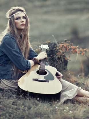 Beautiful hippie girl with guitar sitting on field near stone