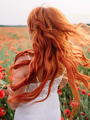 Beautiful young red-haired woman in poppy field with flying hair