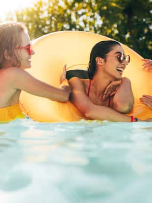 Girls enjoying a day in swimming pool with inflatable ring. Smiling women friends having fun in pool.