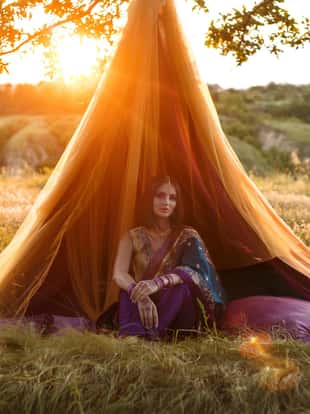Beautiful woman with dark hair Oriental appearance in national costume sits in a unique fairy-tale hut. The image on the backdrop of the beautiful wildlife in the rays of the Golden sunset.Fashionable tinted.Creative color.