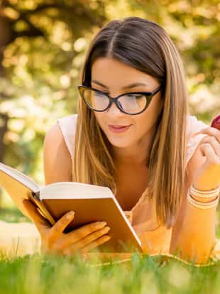 outside portrait of young beautiful woman with apple reading book in park