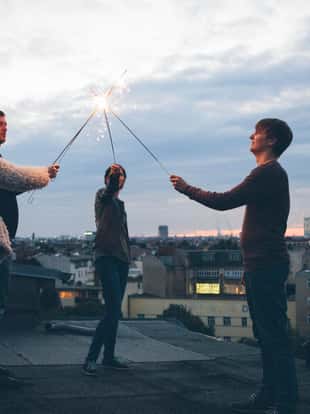 Party: small group of young adults standing on a roof and holding sparklers