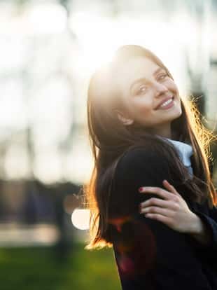 Smiling beautiful woman portrait in sun light on sunset time in city park