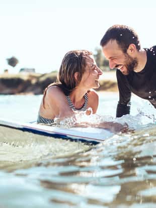 Loving couple of smiling surfers in the water, flirting while waiting for a good wave to come