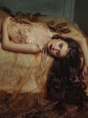 Tale of Sleeping Beauty. The girl is in the old, abandoned room. It covered the dust and leaves. Autumn atmosphere of sadness. Beautiful, long, wavy hair.  Princess lying on the bed and looking at the camera.  Creative colors