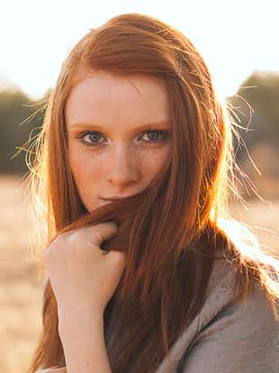 Portrait of Beauty Teenage Model Girl with Red Hair on the Background of Nature on the Field in Sun Light. Face of Young Woman with Freckles. Autumn. Glow Sun, Sunshine. Backlit. Warm Color Tones