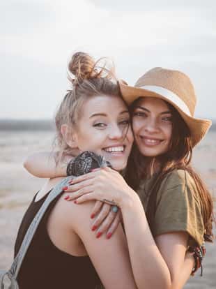 Portrait of smiling young women embracing in desert. Multi-ethnic female friends are standing against sky. They are enjoying vacation together.