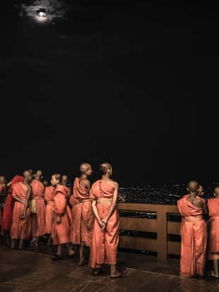 Buddhist monks looking at the full moon at Wat Phra That Doi Suthep the night before Wisaka Bucha in Chiang Mai Thailand. This temple in the outskirts of the city located on the top of a mountain that overlooks the city is a Theravadada Wat was founded in 1383. The Gautama Buddha's shoulder bone is supposed to be housed here as a relic. The night before Vesak or Buddha birthday and enlightenment day thousands of people do a pilgrimage to this temple to celebrate the most important day for buddhists. The festivity takes place on the full moon day of the sixth lunar month.