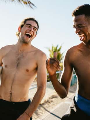 Two cheerful young surfers with surfboards walking and talking along the beach. Men on a holiday going on water surfing.