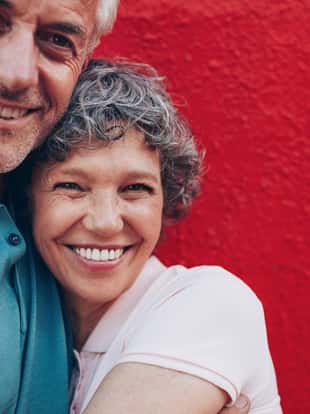 Portrait of cheerful middle aged couple embracing each other against red background. Mature man and woman together against red wall.