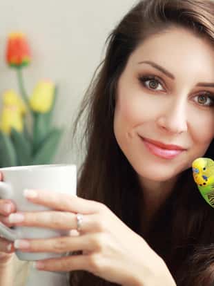 beautiful smiling woman with green parrot on her head beloved pet