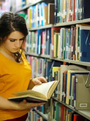 Happy young female student reading book in library