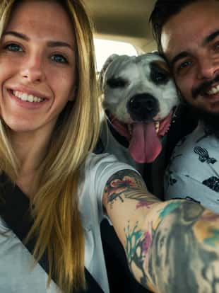 Happy couple making selfie in the car. Their dog posing with them.
