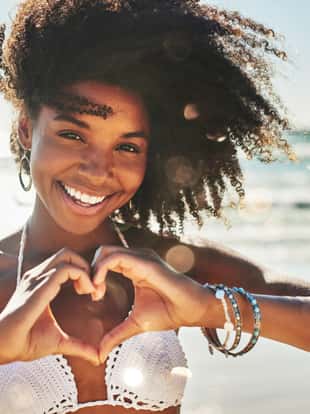 Portrait of a beautiful young woman making a heart shaped gesture with her hands at the beach