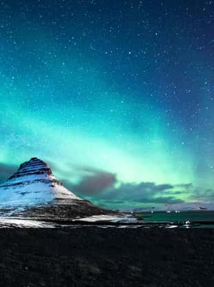Solo traveler walking in front of an awesome Northern Lights in Mount Kirkjufell Iceland.