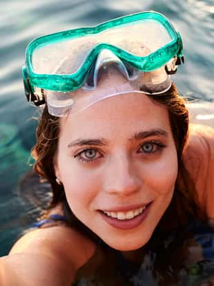 Young woman wearing diving glasses taking selfie looking at camera underwater.