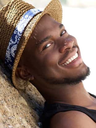 Close up portrait of a smiling young man with hat relaxing outdoors