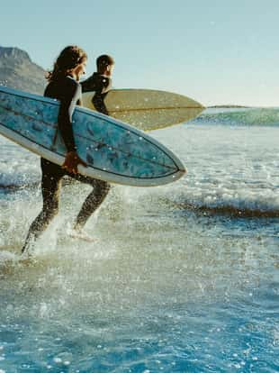 Two male surfers going for surfing in the sea. Two men carrying surfboards running in to the sea for surfing.