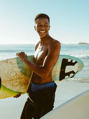 Smiling men walking on the beach carrying surfboards. Male friends on surfing vacation at the sea.