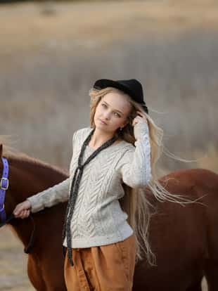 A horse with a young woman in a cowboy hat walks along the mountain steppe