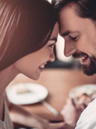 Beautiful couple in love is sitting in cafe face to face and smiling.