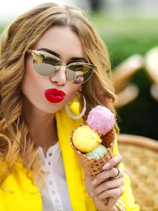 Beautiful blond woman eats ice cream in a cone. The girl in glasses is wearing a yellow bright jacket.