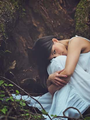Beautiful woman among dark tree roots looks into camera . Mother earth embrace