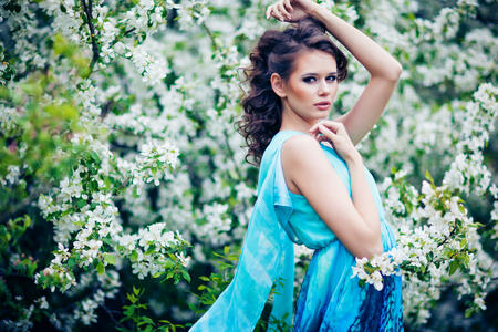 outdoor portrait of a beautiful brunette woman in blue dress among blossom apple trees