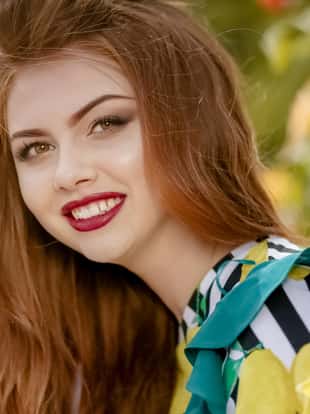 Beautiful young girl with red hair. Hilarious smiling model with beautiful make-up walks down the street