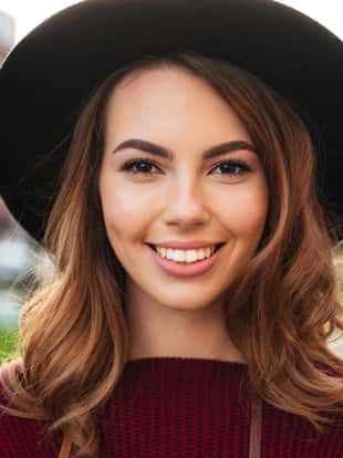 Close up portrait of a beautiful smiling girl with brown hair wearing a hat and looking at camera outdoors