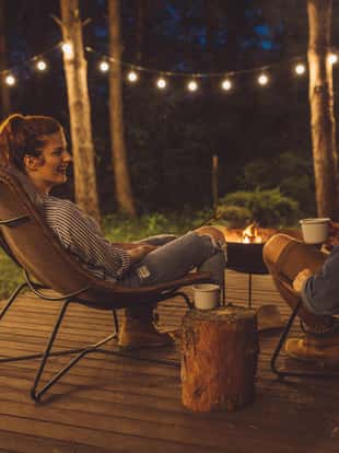 Young couple on vacation in countryside, they enjoy in summer nature. sitting on porch next to the fireplace and have romantic sunset