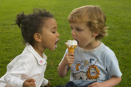 Two young children sharing an ice cream, one a blode boy the other a mixed race girl.