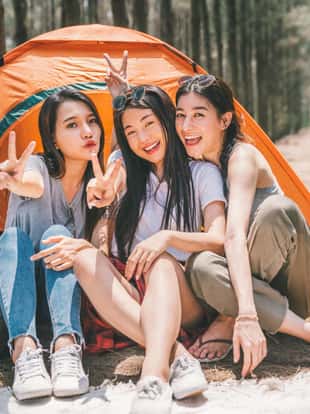 Group of happy Asian teenage girls doing victory pose together, camping by the tent. Outdoor activity, adventure travel, or holiday vacation concept