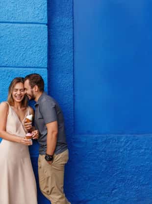 Happy couple in love eating ice cream and smiling against the blue wall
