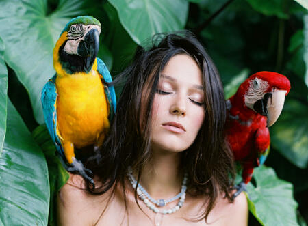 Portrait of young attractive brunette  woman with ara parrots on her shoulders on tropical background.