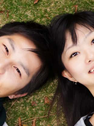 An attractive young Japanese couple laying on their backs on the grass.